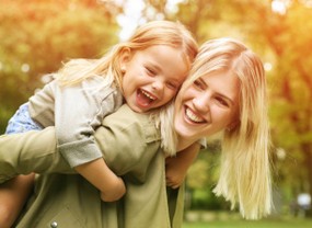 Strength-Based Parenting Program A mother giving her little girl a piggy back ride. Both are laughing and having fun.